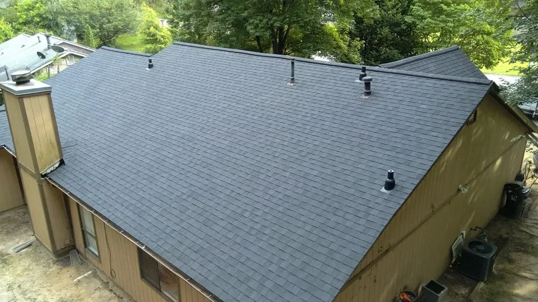 Completed charcoal shingle roof on a ranch home viewed from above, with new pipe boot flashing, chimney flashing and clean hip ridges.
