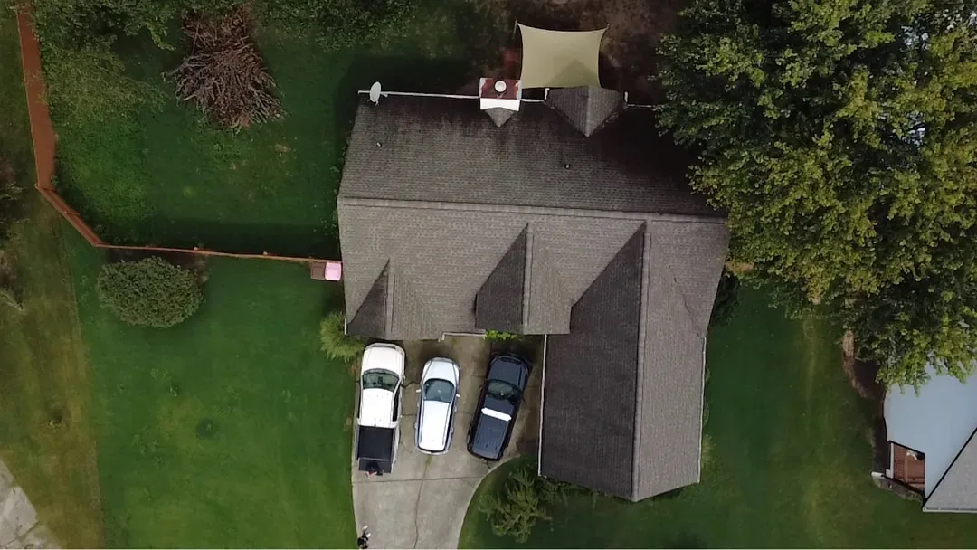 Top-down aerial of a two-storey home before replacement, with an aged brown shingle roof and three vehicles in the driveway.